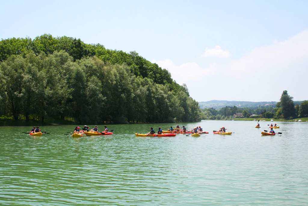 Groupe de personnes en kayak naviguant paisiblement sur le lac de la Gruyère, entourées de verdure luxuriante.