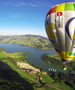 Montgolfière colorée flottant au-dessus du lac de la Gruyère, offrant une vue panoramique sur la magnifique région verdoyante.