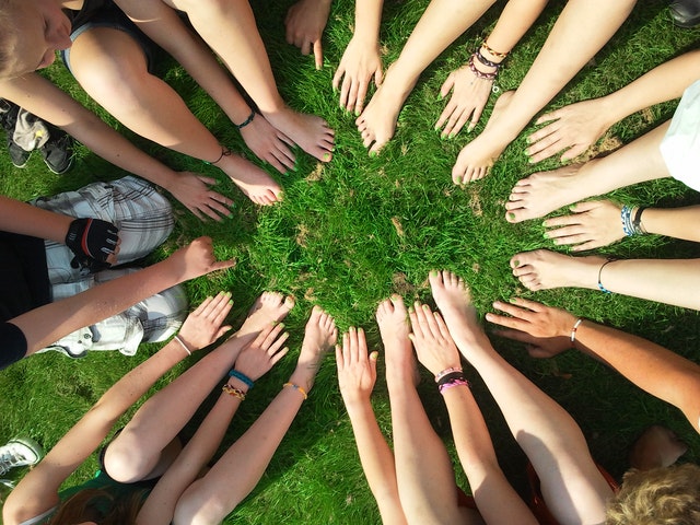 Des main d enfants participant à un camp d été en Suisse romandeUn groupe d'enfants au camp d'été forme un cercle en posant leurs mains sur l'herbe, symbolisant l'unité et l'amitié.